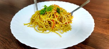 Schezwan Eriştesi ya da sebze Hakka Eriştesi ya da mısır ve domatesli chow mein ahşap bir masada beyaz bir tabakta servis edilir. seçici odak