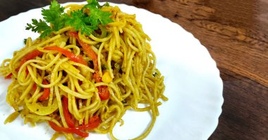Schezwan Eriştesi ya da sebze Hakka Eriştesi ya da mısır ve domatesli chow mein ahşap bir masada beyaz bir tabakta servis edilir. seçici odak