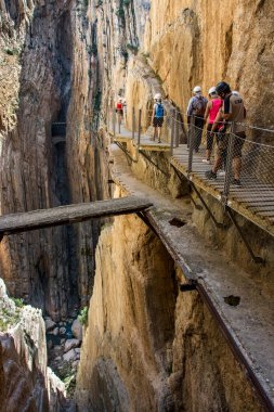Caminito del Rey 'de. Yürüyüşçüler ve turistler antik yola bakan yaya köprüsünde duruyorlar ve Gaitanes geçitlerinin köşeli ve dar kanyonunda