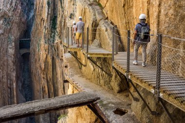 Caminito del Rey 'de. Yürüyüşçüler ve turistler antik yola bakan yaya köprüsünde duruyorlar ve Gaitanes geçitlerinin köşeli ve dar kanyonunda