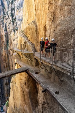 Caminito del Rey 'de. Yürüyüşçüler ve turistler antik yola bakan yaya köprüsünde duruyorlar ve Gaitanes geçitlerinin köşeli ve dar kanyonunda