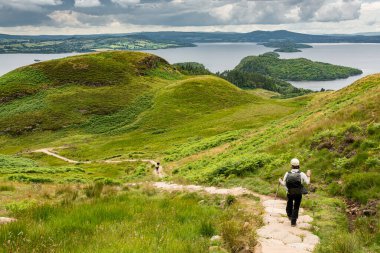 İskoçya, West Highland 'dan Lomond Gölü manzarası. Göle giden yolda yürüyen bir yürüyüşçü.