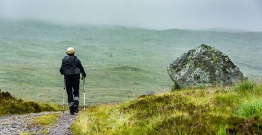İskoçya 'daki Batı Highland Yolu boyunca. Yürüyüşçünün biri, bir kayanın yanındaki eski bir askeri yoldan geçen yürüyüş yolunda yürüyor..
