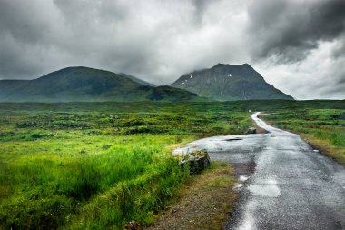 Batı Highland Yolu boyunca. Yağmurla ıslanmış küçük bir yol Stob 'a doğru gidiyor gibi görünüyor. Bulutlardan çıkan bir Ghlais Choire dağı.