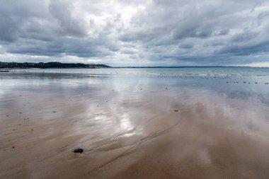 Bulutlu ve tehditkar bir gökyüzü, yağmurlu bir günde Kuzey Britanya 'da bir kumsalın ıslak kumlarına yansıyor.