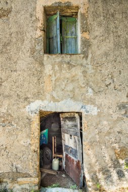 Yıpranmış duvarları olan eski bir evin tamir edilmiş kapısı ve yorgun kepenkleri.