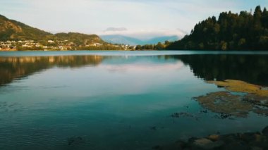 Rocky beach on a lake in Norway. Green mountains in the background. Side flight.