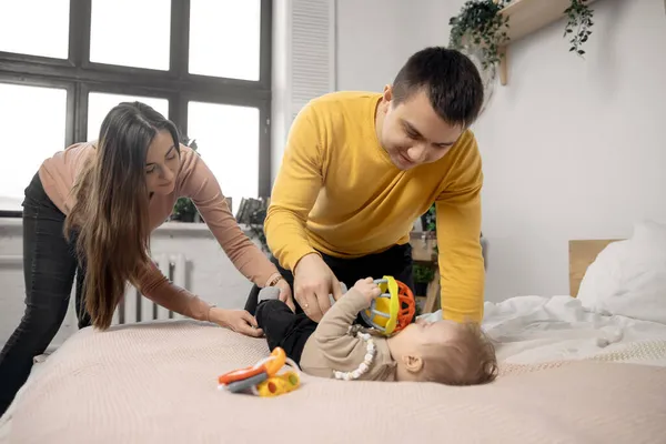 Родители занимаются гимнастикой с малышом на кровати, концепция молодой семьи — стоковое фото