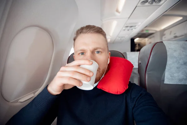 Hombre bebe agua pasajero de avión, disfruta de almohada para dormir en silla. Concepto de viaje con máscara segura — Foto de Stock