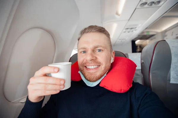 Manliga passagerare i flygplan dricker vatten innan start njuter av kudde för att sova i stol. Begreppsresa med säker mask — Stockfoto