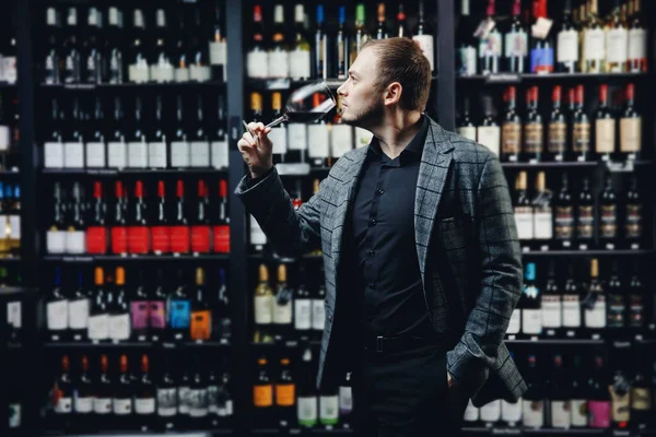 Портрет сомелье мужчина с бокалом красного вина на фоне витрины алкогольного магазина — стоковое фото
