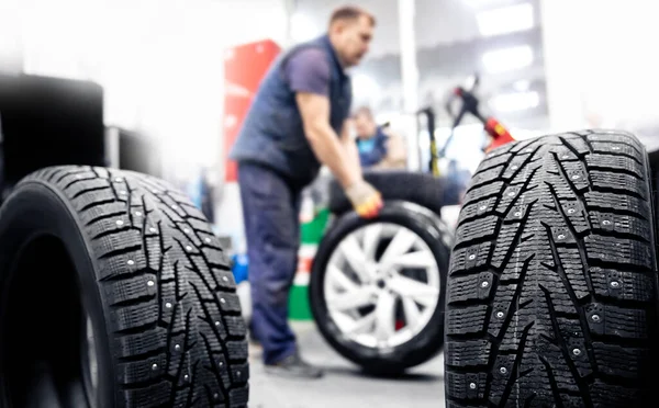 Koncepce autoservis výměna zimních a letních pneumatik. Mechanik drží kola v garáži — Stock fotografie