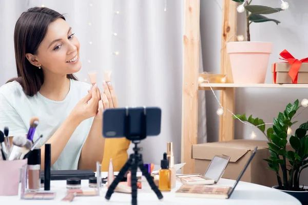 Blogger belleza principiante, mujer joven, hace revisión de la fundación para la piel, escribe blog para suscriptores en el teléfono —  Fotos de Stock