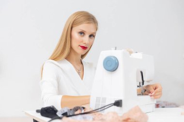 Dikiş makinesiyle yakın çekim işlemi, moda tasarımcısı çerçeveye bakıyor