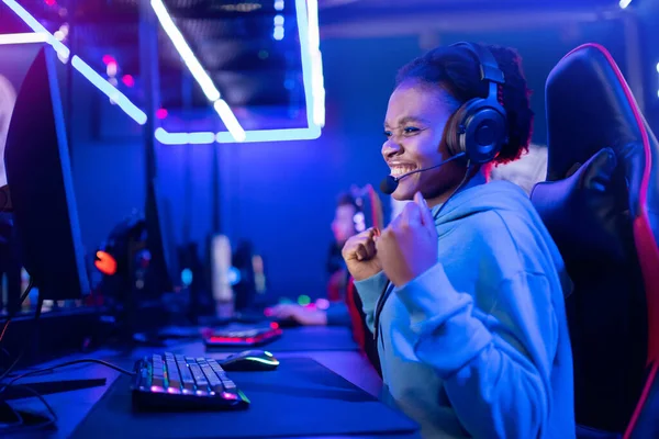 Joven americana africana sonrisa mujer profesional jugador ganar en línea de videojuegos con auriculares, fondo de neón —  Fotos de Stock