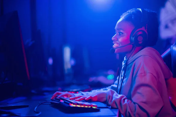 Streamer mujer joven africana se regocija en la victoria jugador profesional jugando juegos en línea ordenador con auriculares, color neón —  Fotos de Stock