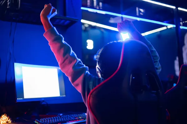 Streamer africká mladá žena se raduje z vítězství profesionální hráč hraje online hry počítač se sluchátky, pohled zezadu — Stock fotografie
