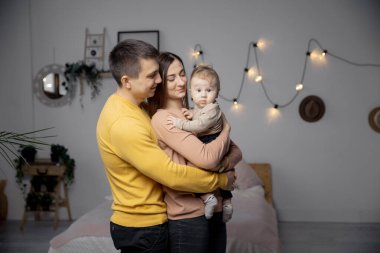 Mutlu bir aile kadını, erkek ve çocuk yatakta oturuyor ve gülümsüyor.