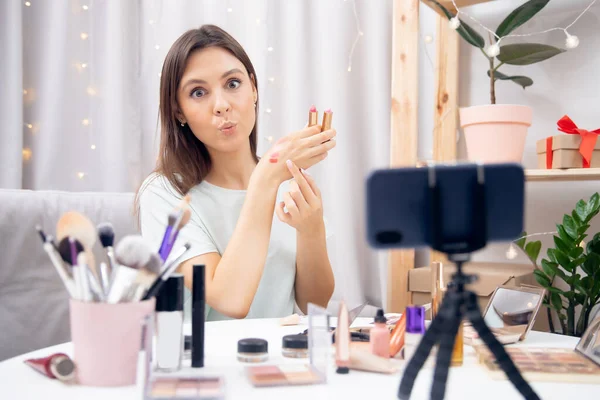 Happy woman vlogger es revisar cosméticos lápiz labial grabación de flujo de vídeo en el teléfono. Concepto Influencer blogger beauty blog —  Fotos de Stock