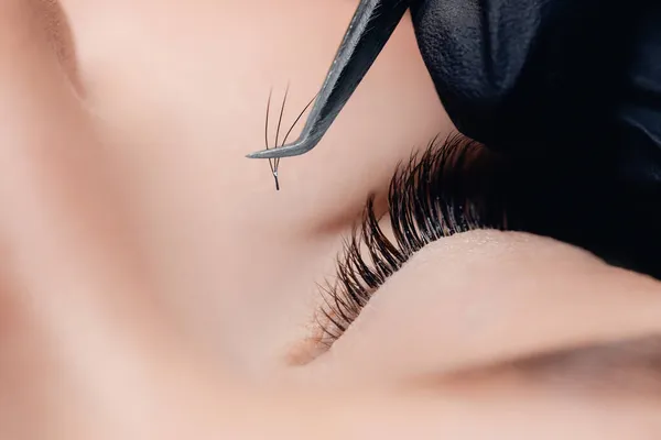 Szempilla hosszabbítási eljárás. Mester csipeszek fekete hamis hosszú szempillák gyönyörű női szemek — Stock Fotó