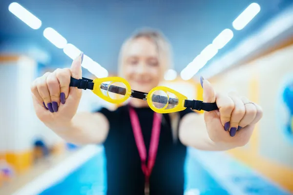 Плавальні окуляри в руках жінки-тренера на фоні басейну — стокове фото