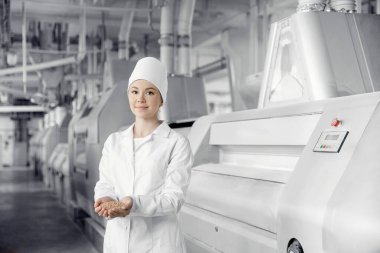Modern ekipmanların arka planında fabrika mühendisi un değirmeni, elinde buğday taneleri tutan kadın.