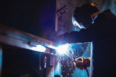 Profesyonel kaynakçı çelik yapı imalat fabrikasında çalışıyor, mavi renk.