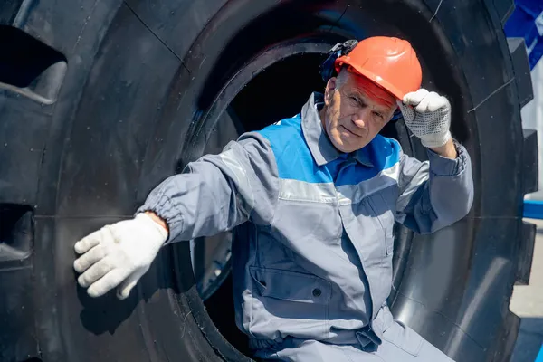 Retrato conceptual del hombre en la fábrica. Conductor de camión en planta industrial se sienta en el neumático del coche — Foto de Stock