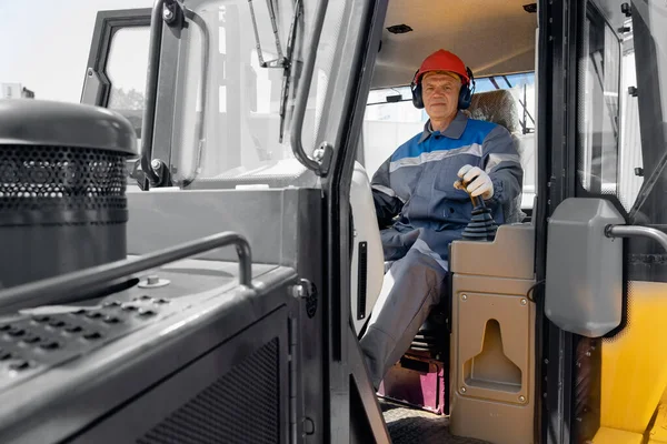 Szczęśliwy kierowca wywrotki przemysłowej siedzi w kabinie i pracuje na placu budowy — Zdjęcie stockowe