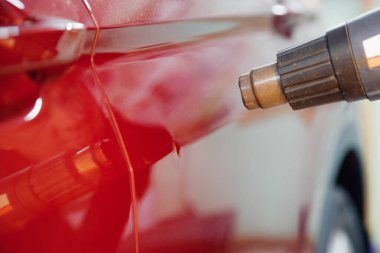 Usta oto tamircisi, benzin istasyonundaki araba gövdesindeki çöküntüleri ve kusurları gidermek için saç kurutma makinesiyle metal ısıtıyor.