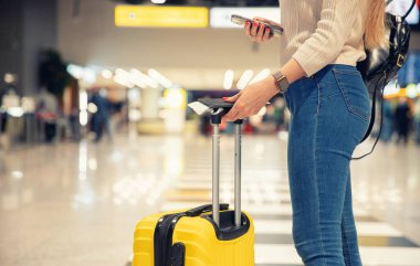 Elinde telefon ve sarı valizli, pasaportlu ve uçak bileti olan genç bir kadın.