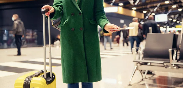 Concepto bandera avión de viaje en otoño. Mujer sin rostro en abrigo verde tiene pasaporte con billete y maleta amarilla aeropuerto — Foto de Stock