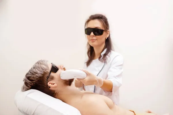 Female worker depilates hair of man on face with laser machine in spa salon — Stock Photo, Image