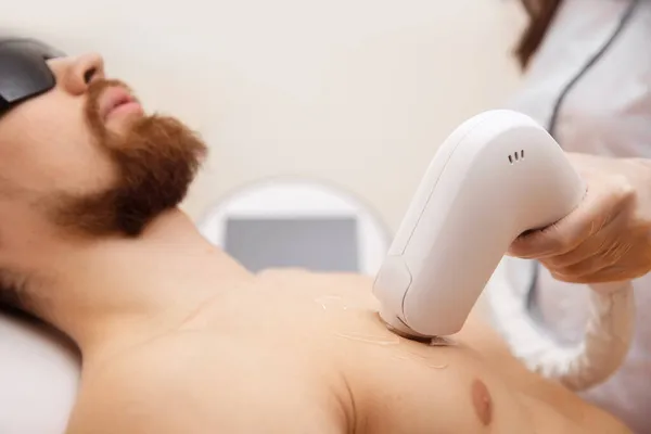Концепція лазерної депіляції для чоловіків. Працівник салону краси застосовує лікування хлопця для видалення волосся на тілі — стокове фото