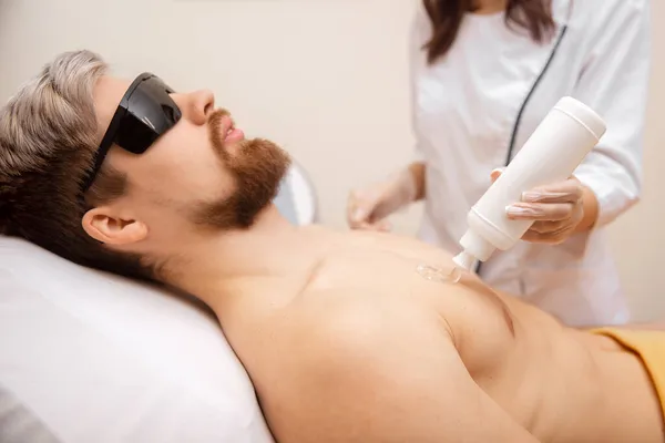 Concetto di depilazione laser per uomini. Salone di bellezza lavoratore applica gel al corpo ragazzo prima della depilazione — Foto Stock