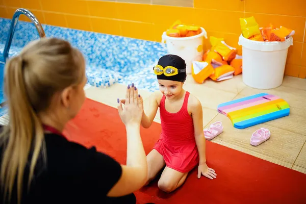 Team woman coach and kid athlete in pool, swimming training school for children
