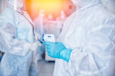 Termometre kontrollü hemşire ekibi kliniği koruyucu giysiler ve maskeli hastaları kontrol ediyor. Kırmızı bölgede 19 Coronavirus bayrağı var.