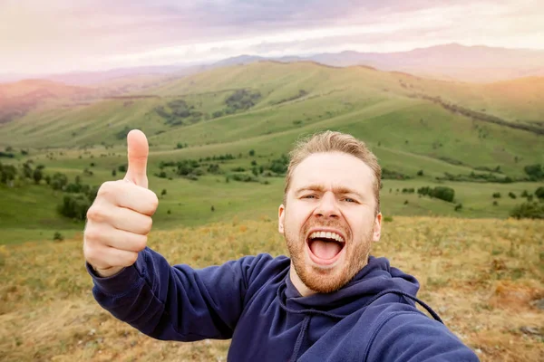 Счастливый молодой человек блоггер на фоне гор на летнем закате. Стиль жизни скандинавский путешественник делает селфи фото — стоковое фото