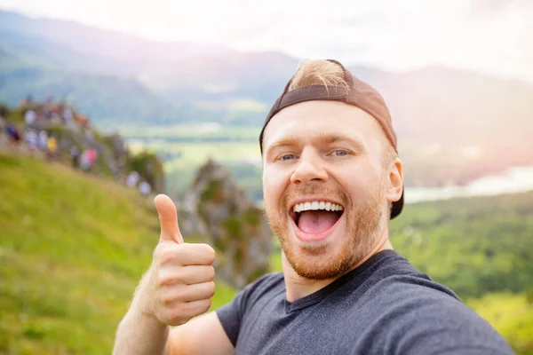 Ung lycklig man resenär gör selfie på bakgrunden av bergen i solnedgången. Begreppet äventyr resa semester — Stockfoto