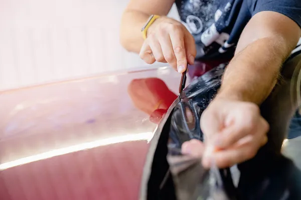 Proceso de pegado de capucha de coche rojo con película de vinilo protectora de astillas de grava y arañazos. Protección transparente para la pintura —  Fotos de Stock