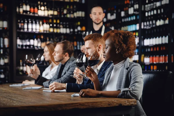Degustación de vinos tintos en restaurante con sommelier. Grupo de amigos europeos y africanos son el alcohol degustación — Foto de Stock