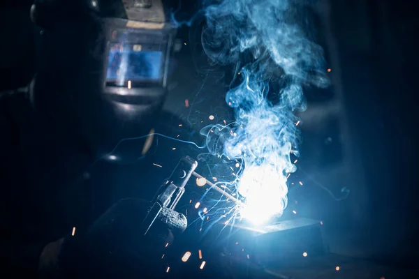 Промисловий працівник зварювальник на заводі використовує маску обладнання та інструмент для роботи з металом з димом, вогнем, іскрою — стокове фото