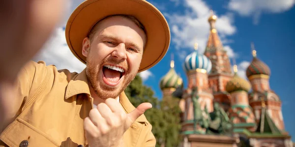 快乐的年轻人带着棕色的帽子在莫斯科克里姆林宫红场自拍旅行。前往俄罗斯的概念横幅旅行 — 图库照片