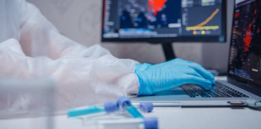Beyaz tehlikeli madde koruyucu araştırma uzmanı modern laboratuarda bilgisayar kan testi üzerinde çalışıyor. Mavi renk, korona virüsü salgını