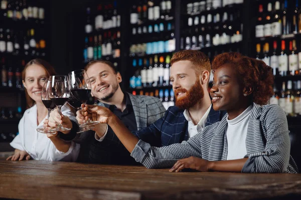 Mujer africana y los hombres europeos se mezclan con copas de vino tinto en el restaurante. Concepto Amistad multicultural — Foto de Stock