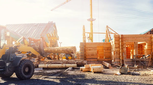 Carregador carrega logs contra o fundo da construção de casa de madeira — Fotografia de Stock