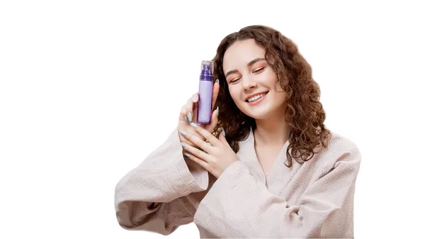 Szczęśliwa młoda kręcone kobieta trzyma butelkę z kosmetyki produktu do pielęgnacji skóry odizolowany biały. Koncepcja kosmetologii przeciwko trądzikowi — Zdjęcie stockowe