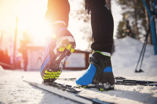 Спортсмен готується до катання на лижах по пересіченій місцевості взимку, закріплюючи черевики сонячним світлом — стокове фото