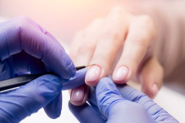 Manikürcü kadın hasta tırnağına jel cilası sürmek için ince fırça kullanır, konsept manikür