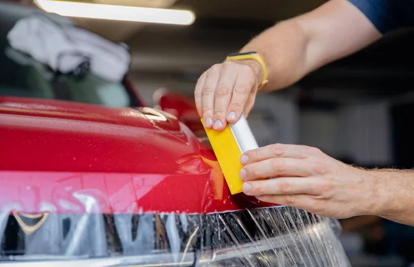 Proces lepení kapoty červeného automobilu ochranným vinylovým filmem ze štěrkových štěrbin a škrábanců. Průhledná ochrana pro nátěr — Stock fotografie